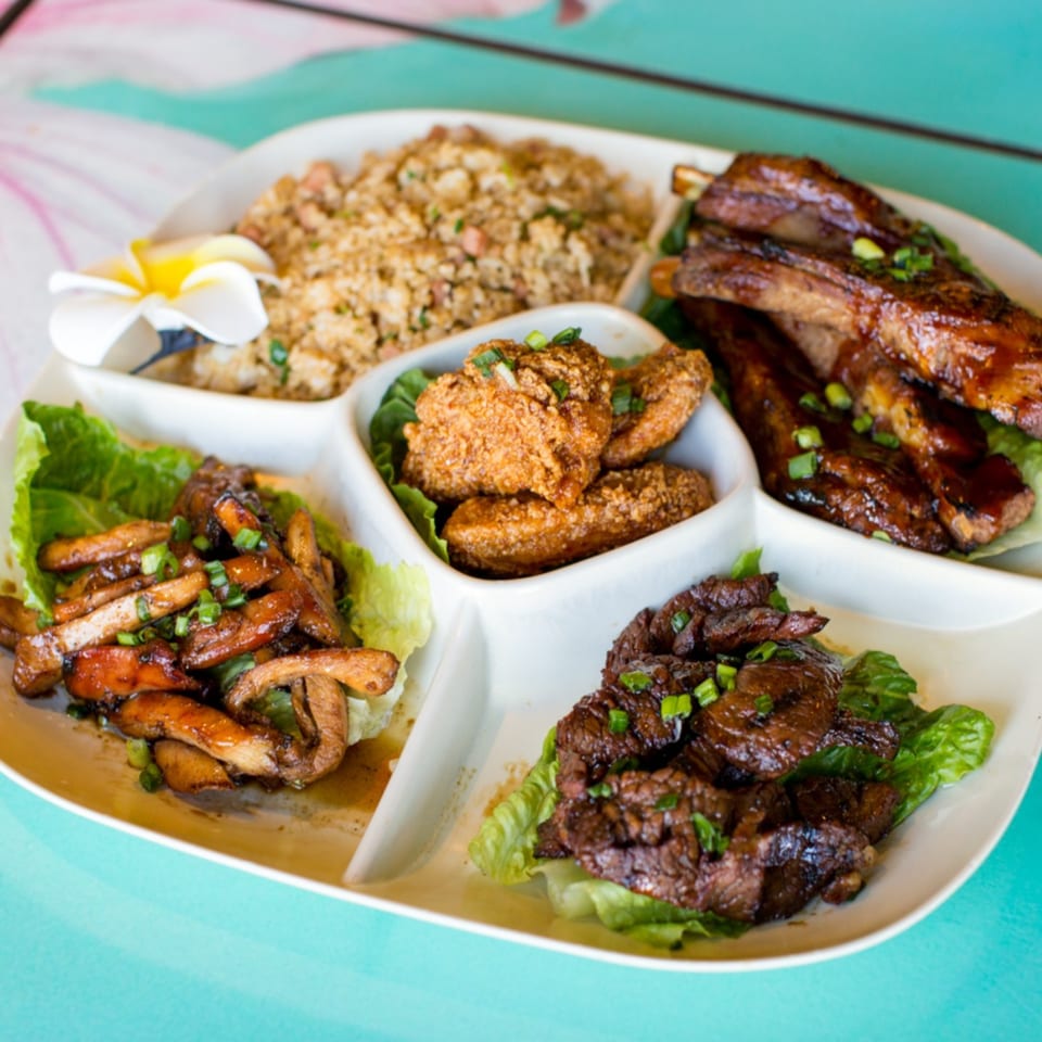 A white platter with sections of fried rice, ribs, fried chicken, and stir-fried meat.