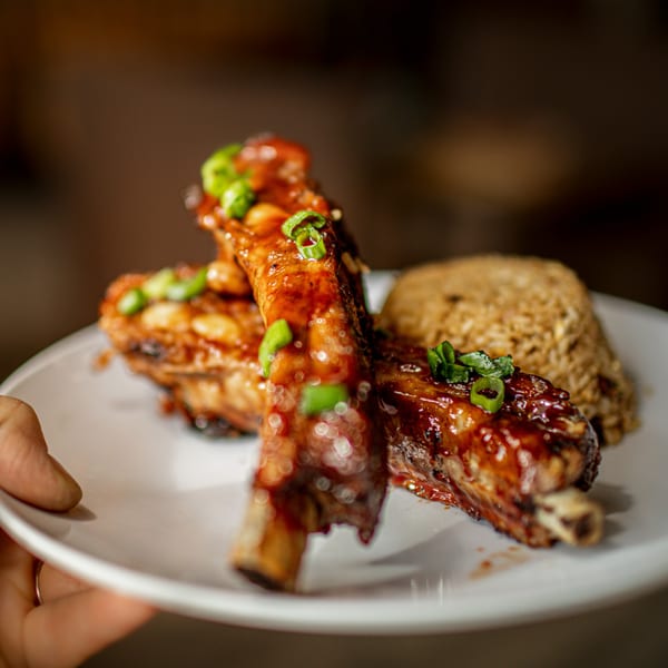Hula Pizzeria & Grill's BBQ ribs with rice, garnished with green onions, on a white plate.